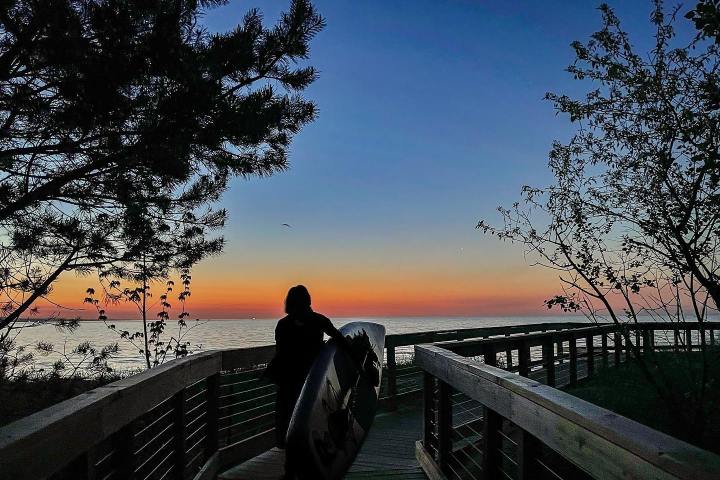 person carrying a paddleboard to the beach during sunrise