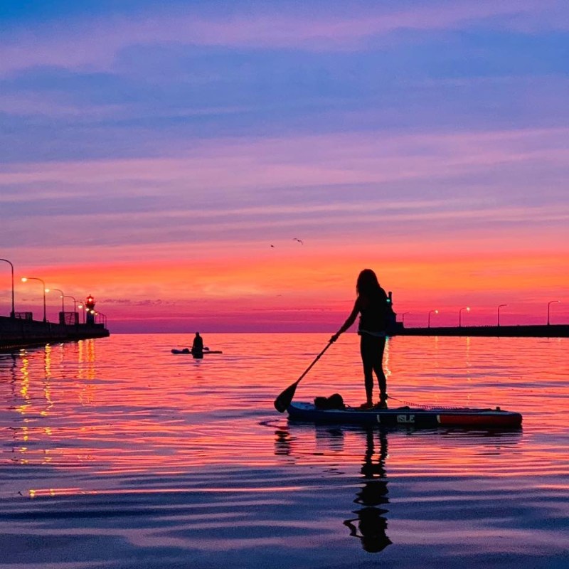 a man standing in front of a sunset over a body of water