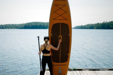 woman standing on a dock holding up a Paddle North paddleboard and a paddle