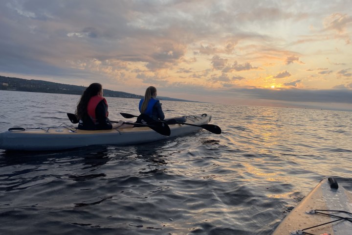 two kayakers in a tandem kayak looking at sunset