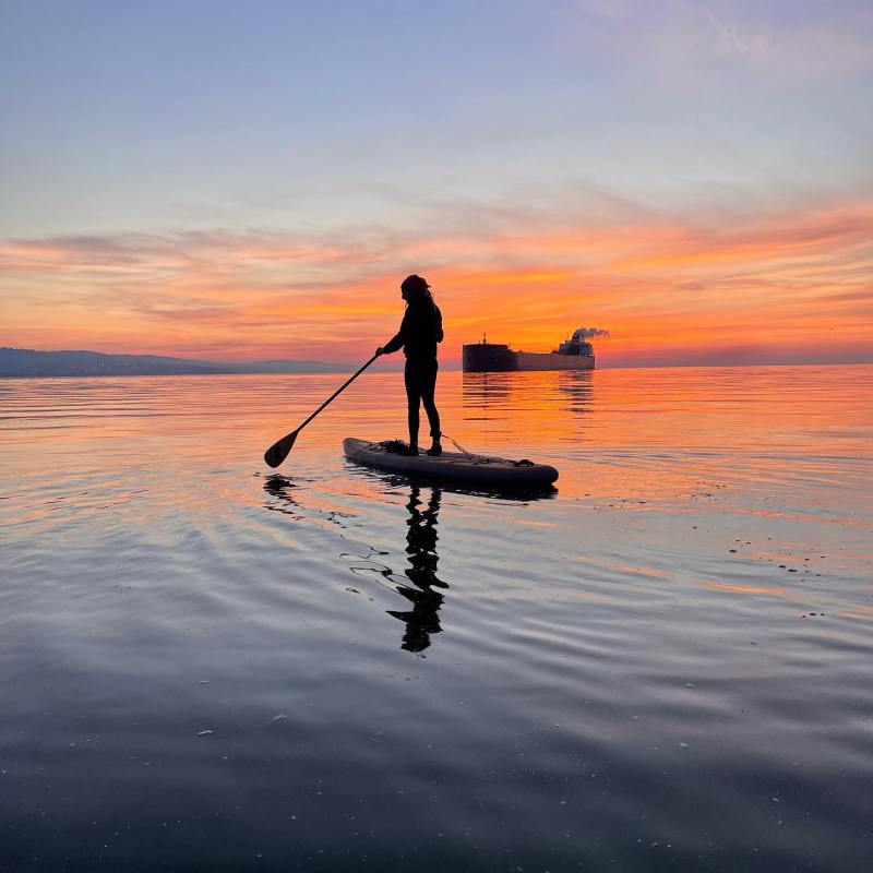 paddleboarder during sunrise paddling by a freighter