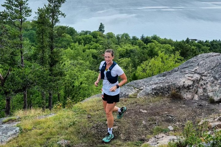 Person trail running on a rocky path with trees and a lake in the background.