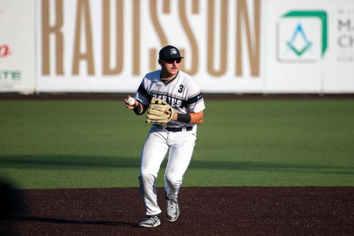 Baseball player in white uniform holds ball and glove, running on field with Radisson signage behind.