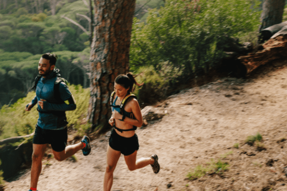 Two people trail running through a forest on a sunny day.