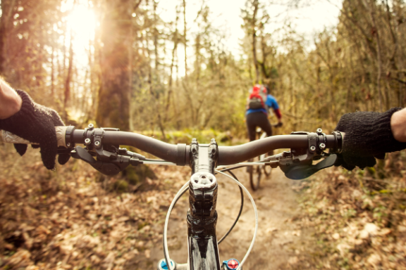 POV of mountain biking on a forest trail with two cyclists ahead.