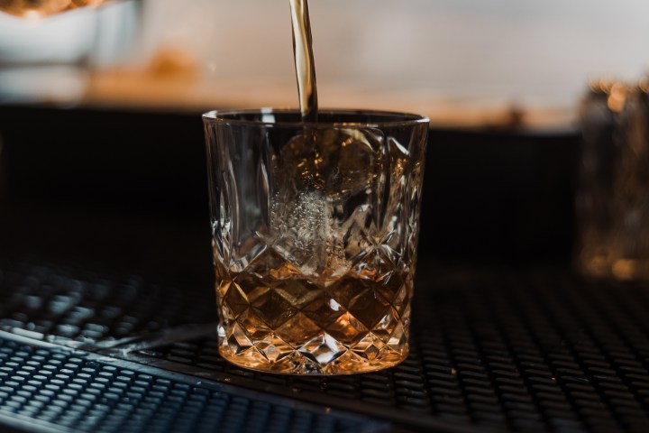 Brown liquid being poured into a crystal glass on a bar counter.