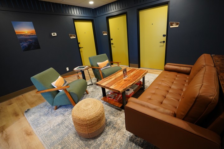 Cozy lounge area with brown sofa, two green chairs, wooden table, and yellow doors on blue walls.
