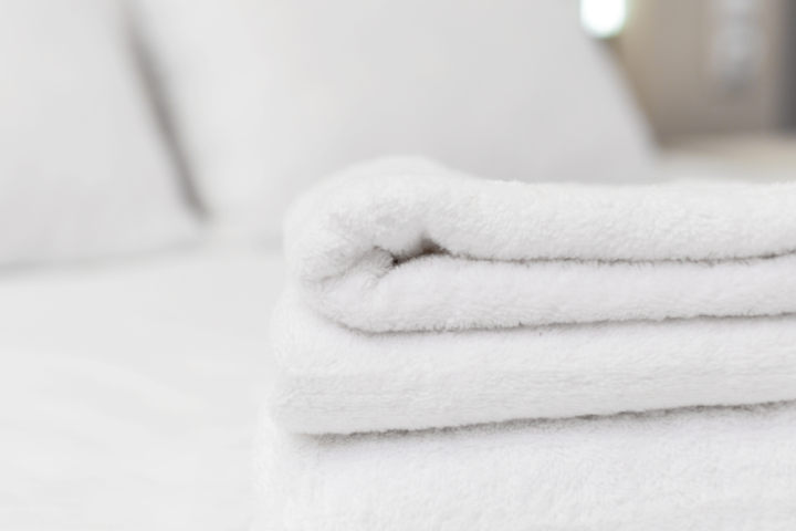 Stack of folded white towels on a bed in a room.