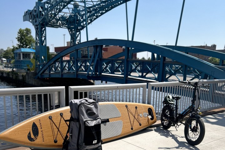 Paddleboard, backpack, and bike next to a blue drawbridge over water on a sunny day.