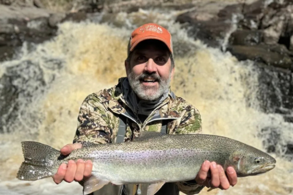 man holding a fish in front of a waterfall