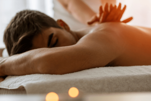 Person receiving a back massage on a white towel with lit candles in the foreground.