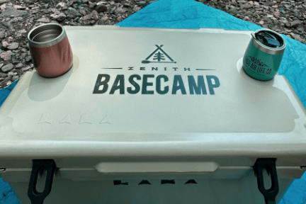Cooler labeled 'Zenith Basecamp' with two cups on top, set on a blue surface.